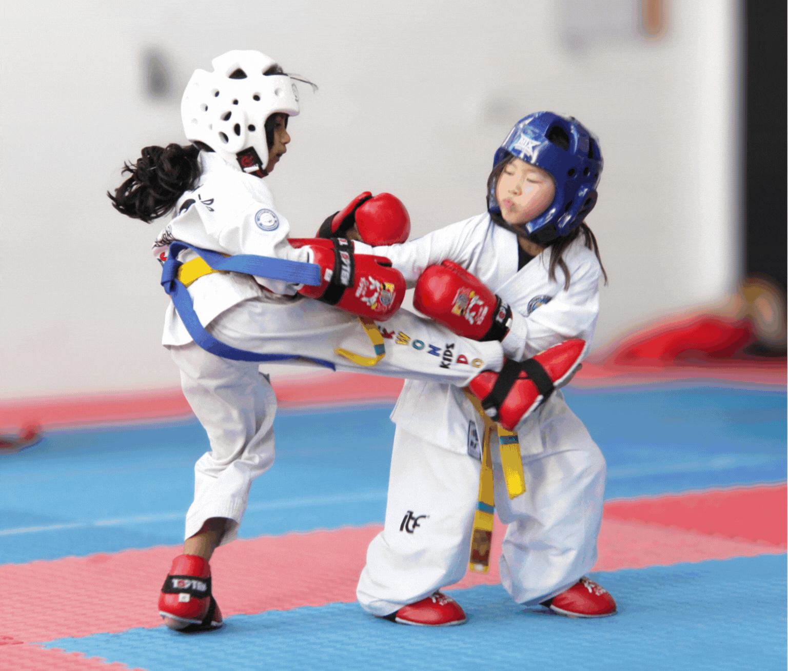 Two taekwondo sparring children in white uniforms and red gloves on a blue mat