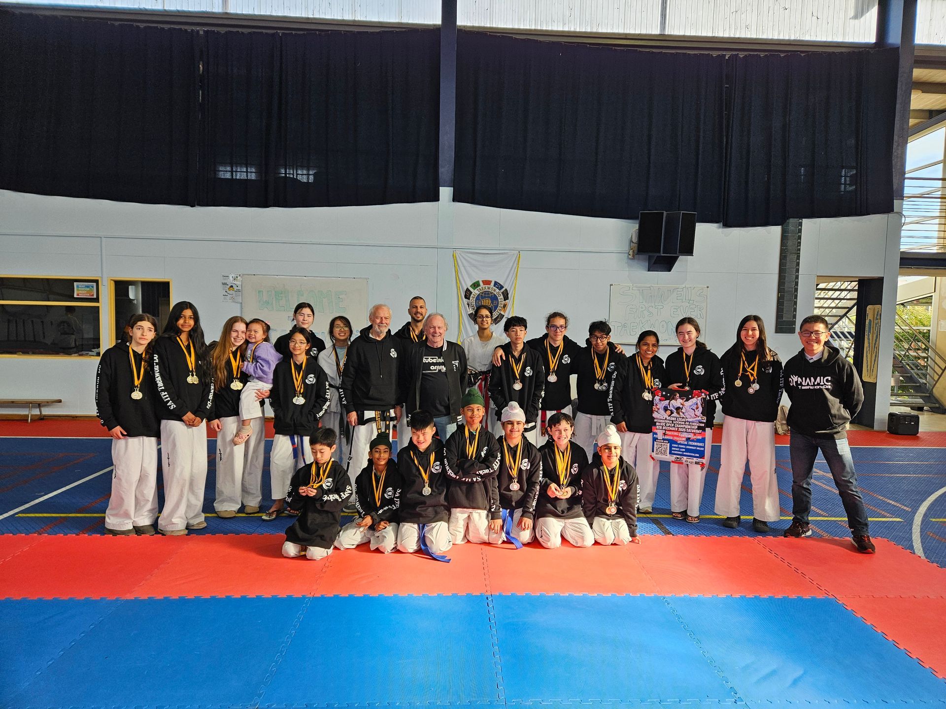 Group posing for a team photo on a blue-and-red gym mat, with a banner in the background.
