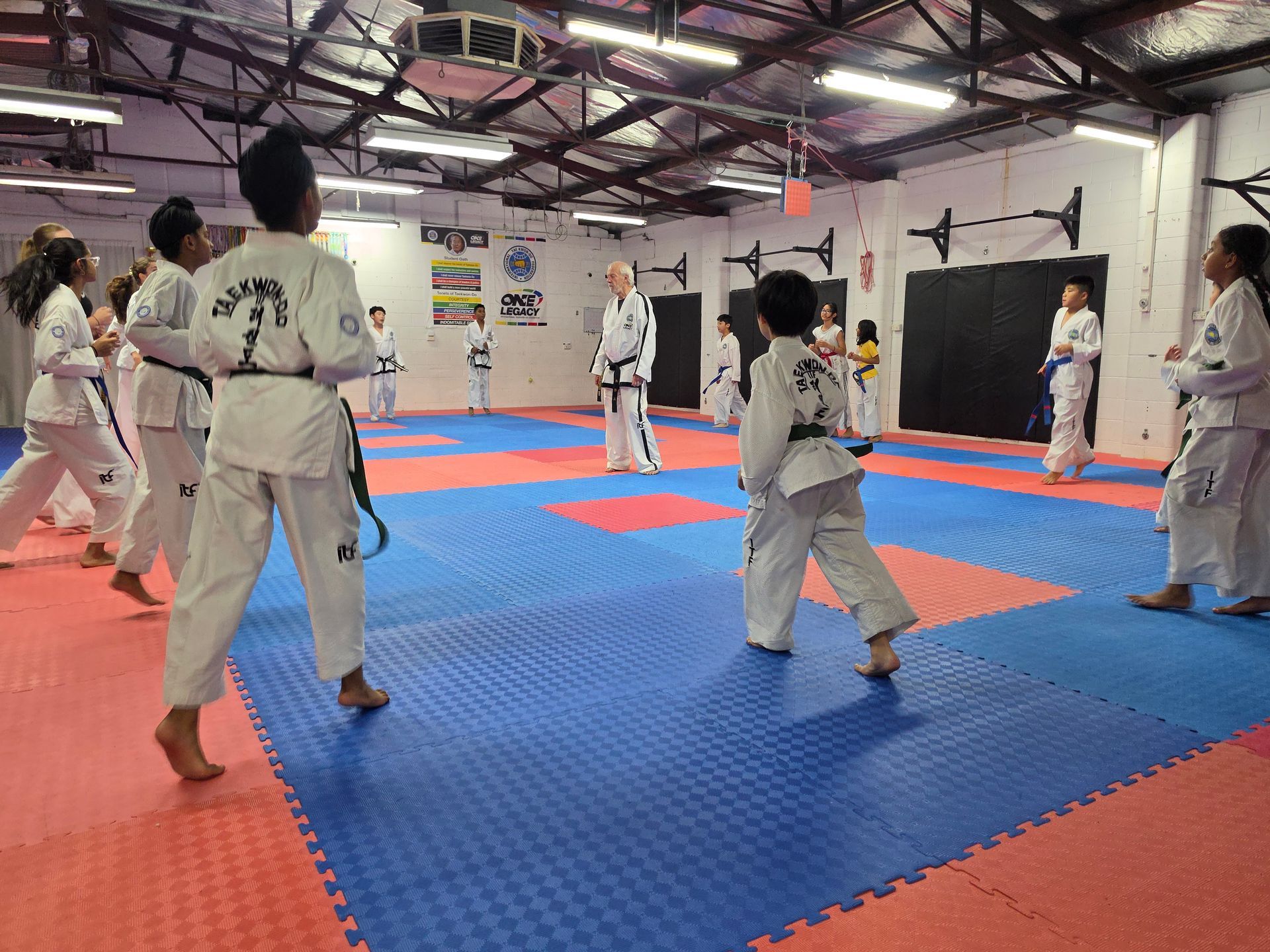 People practicing martial arts in a dojo on blue and red mats under bright overhead lights.