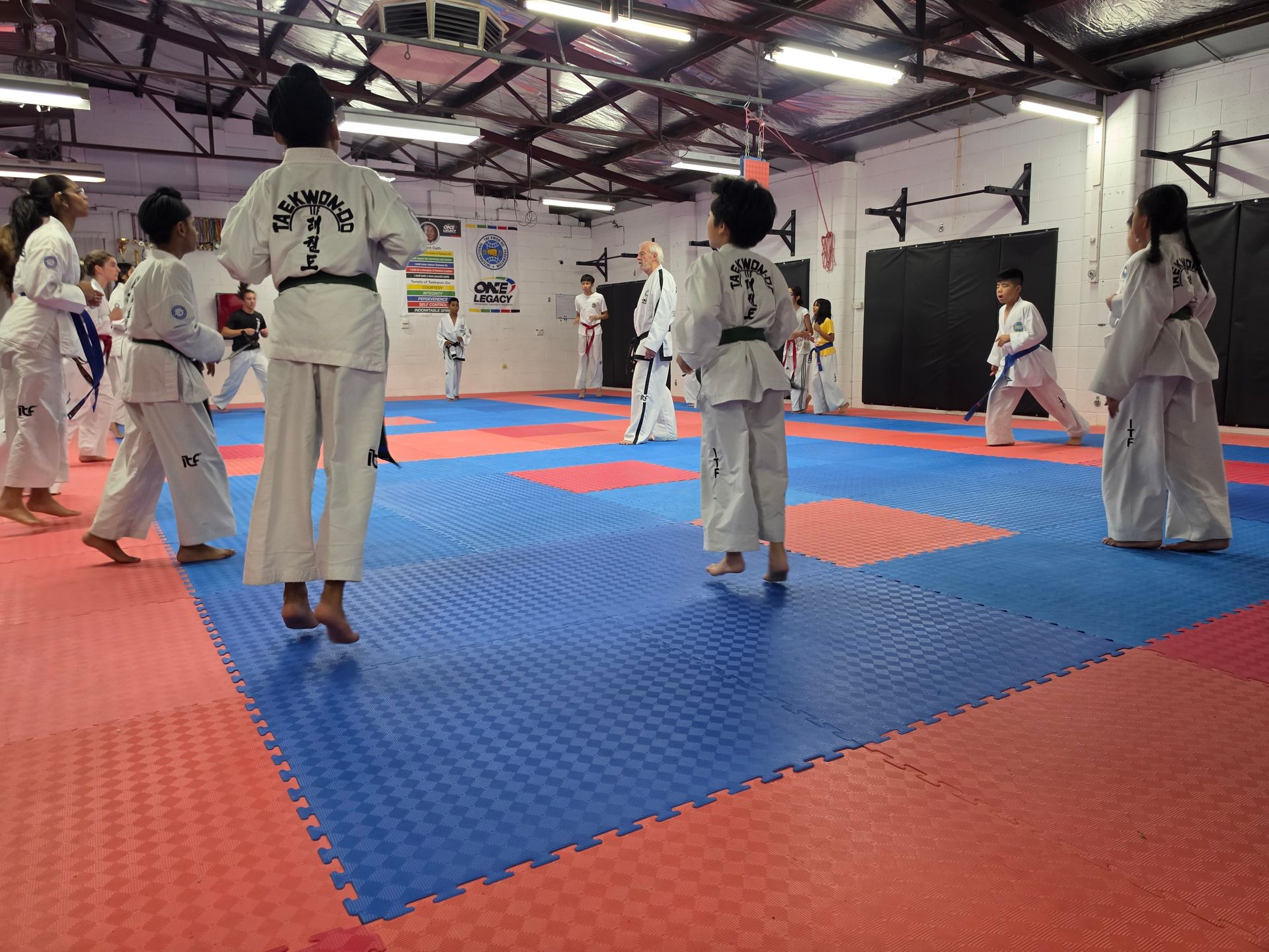 People in white martial arts uniforms practicing on blue and red mats in an indoor gym.