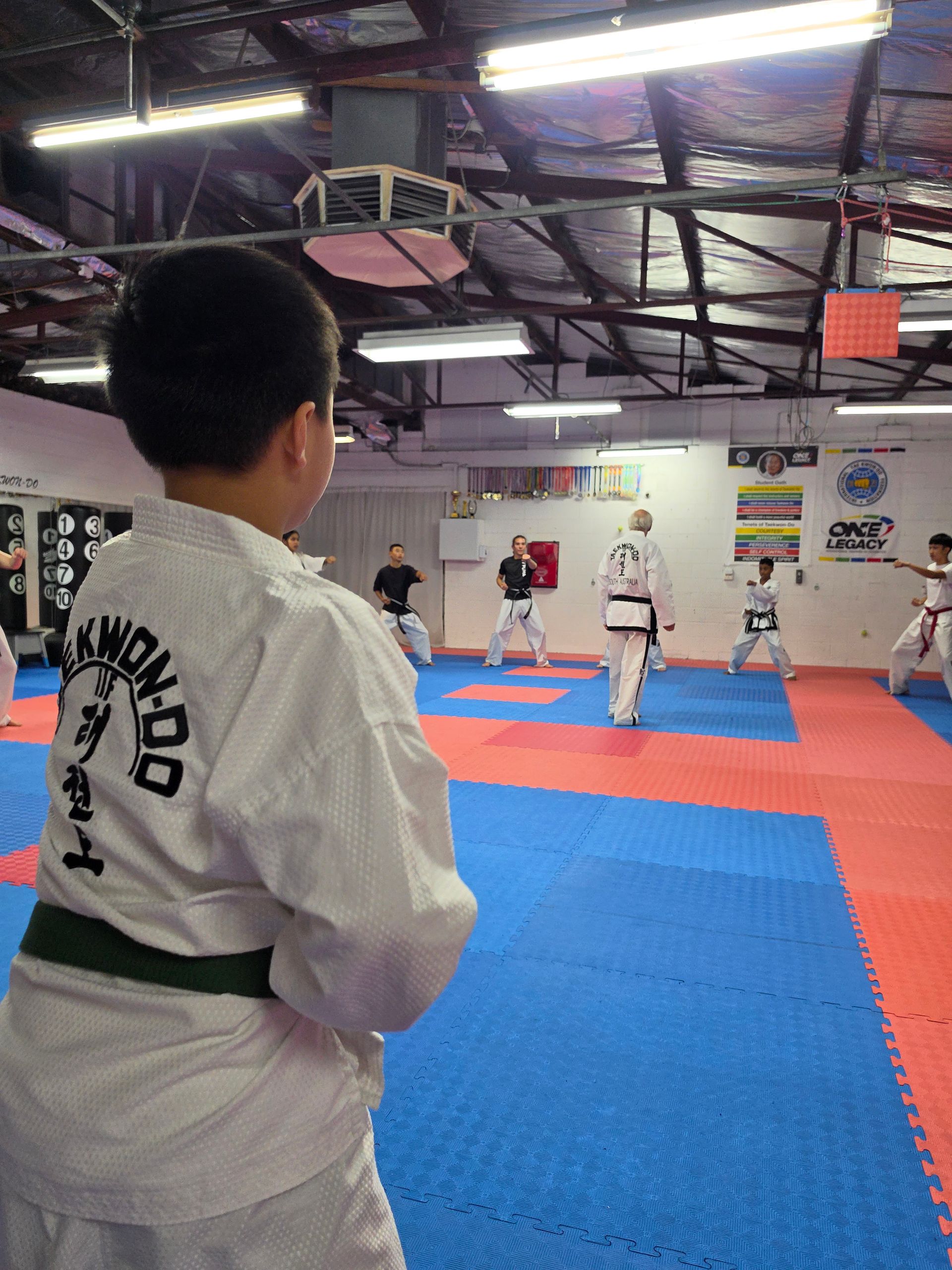 Martial arts class on blue and red mats, with students in white uniforms practicing in a gym.
