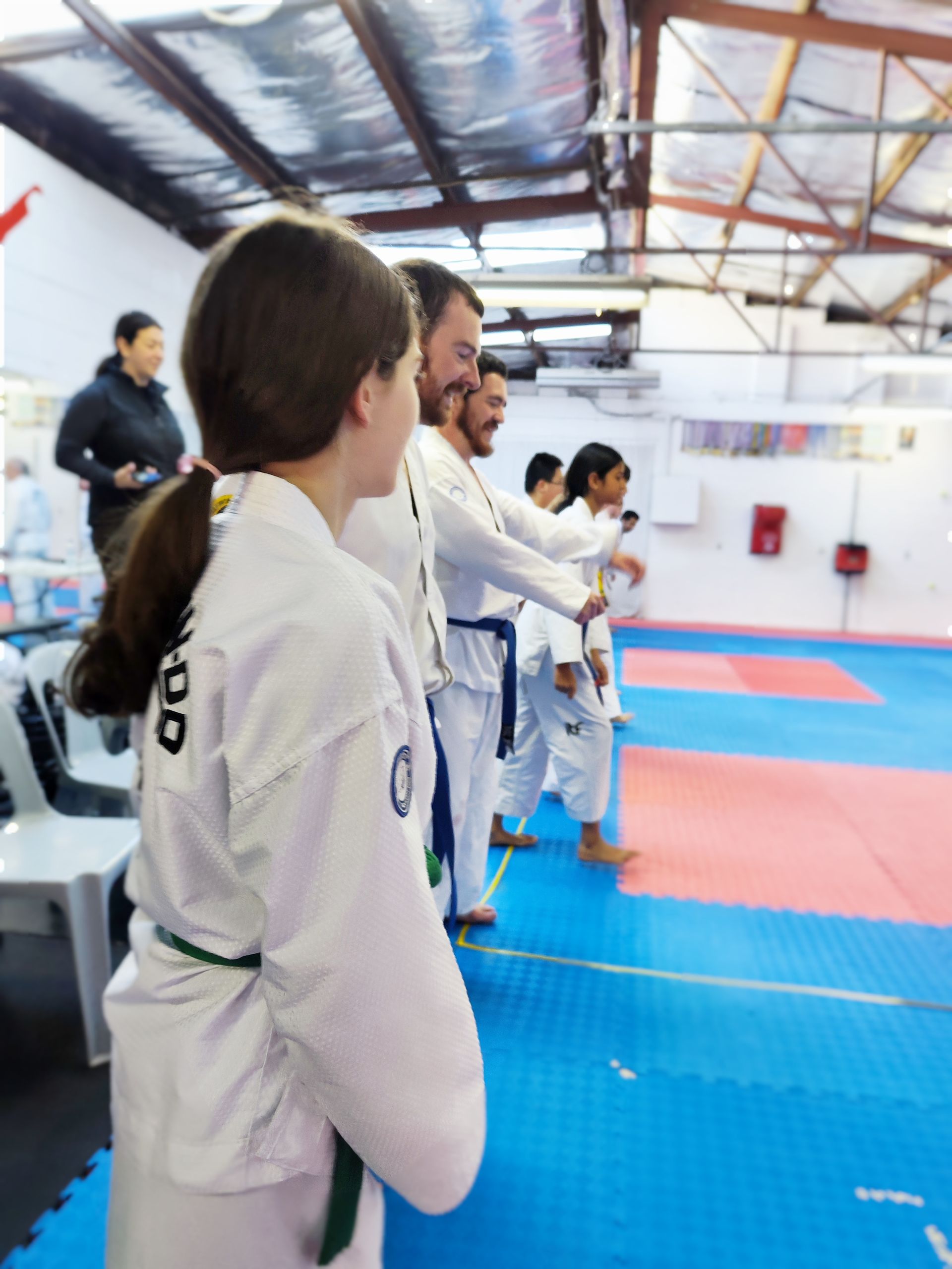 Martial arts students in white gis standing in line on blue and red mats indoors