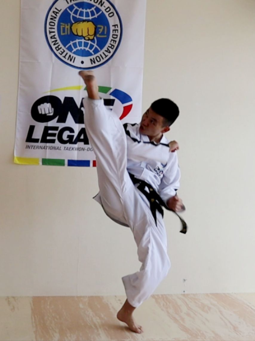 Two taekwondo competitors sparring, one in red gear kicking a blue-geared opponent on a mat