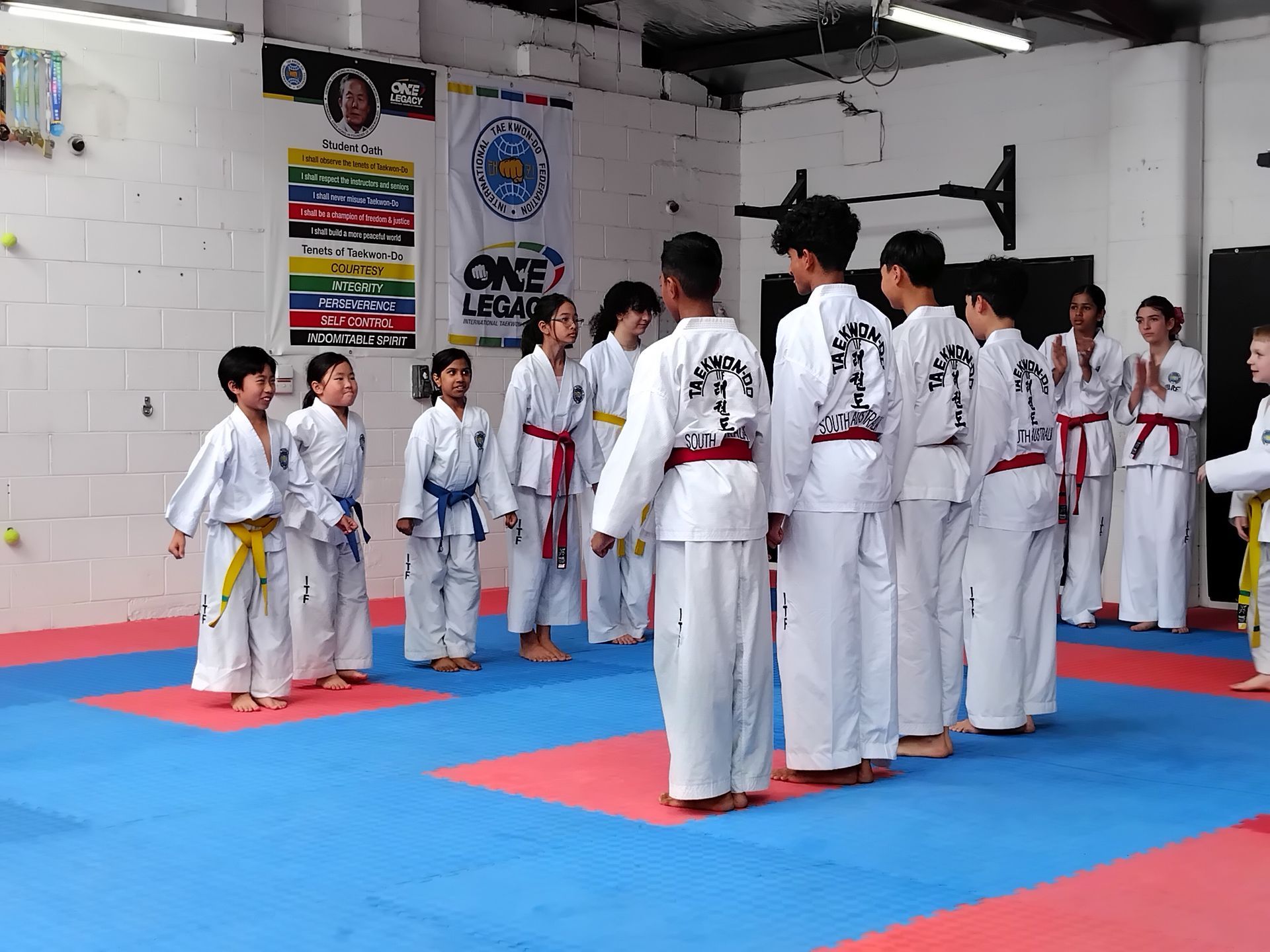 Martial arts class in white uniforms standing on blue and red mats in a dojo