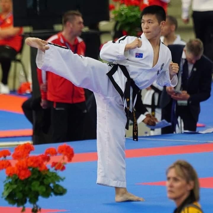 Martial artist in white gi performs a high side kick on a blue competition mat