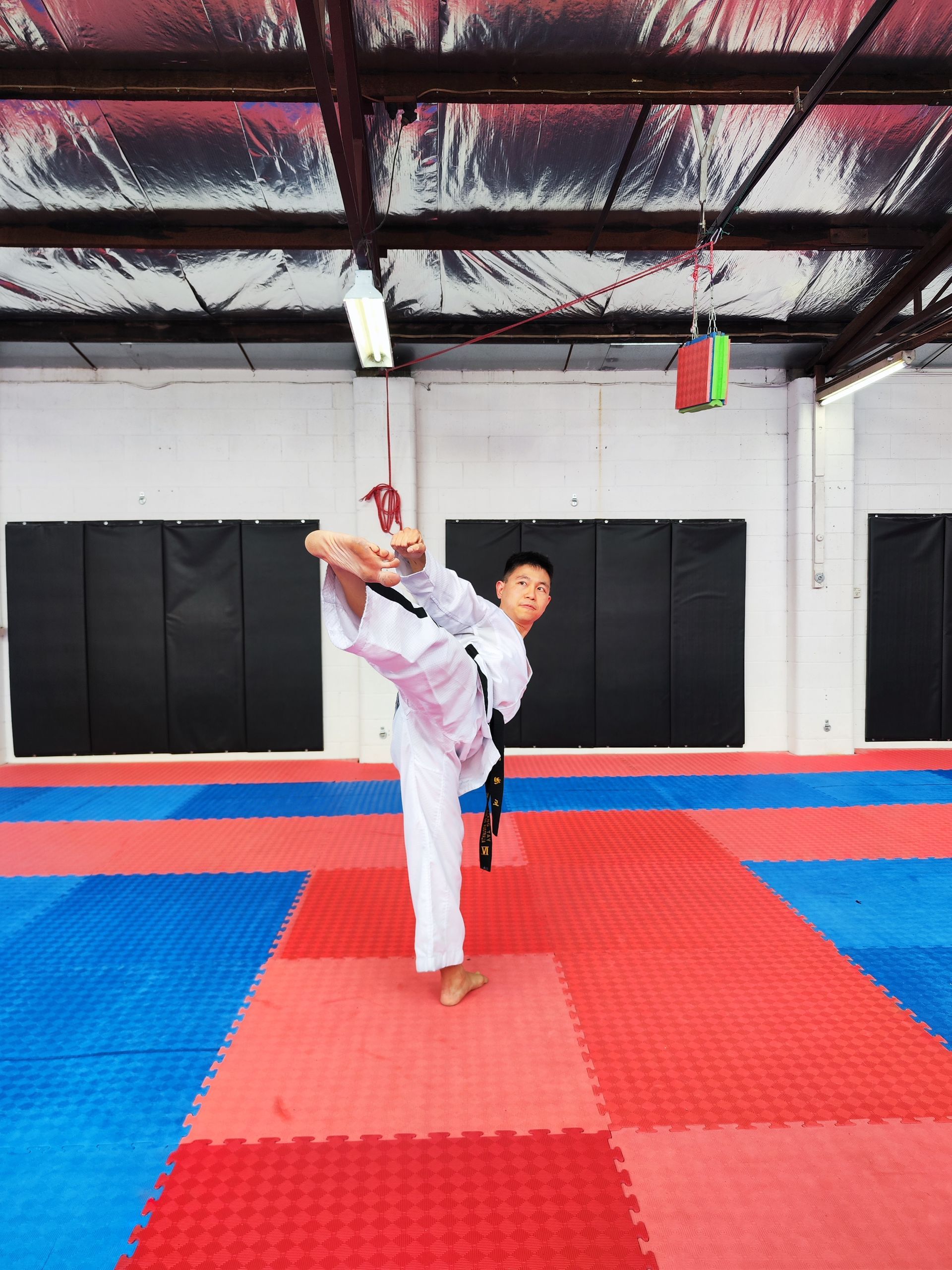 Martial artist in white uniform performing a high kick on red and blue mats in a gym