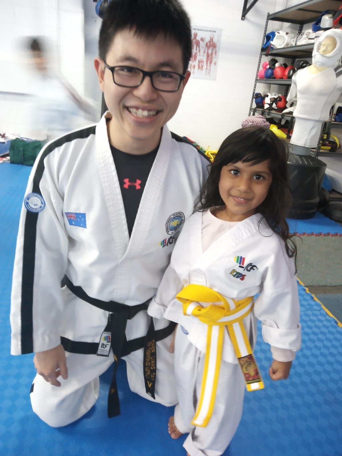 Two martial artists in white uniforms and yellow belts smiling indoors