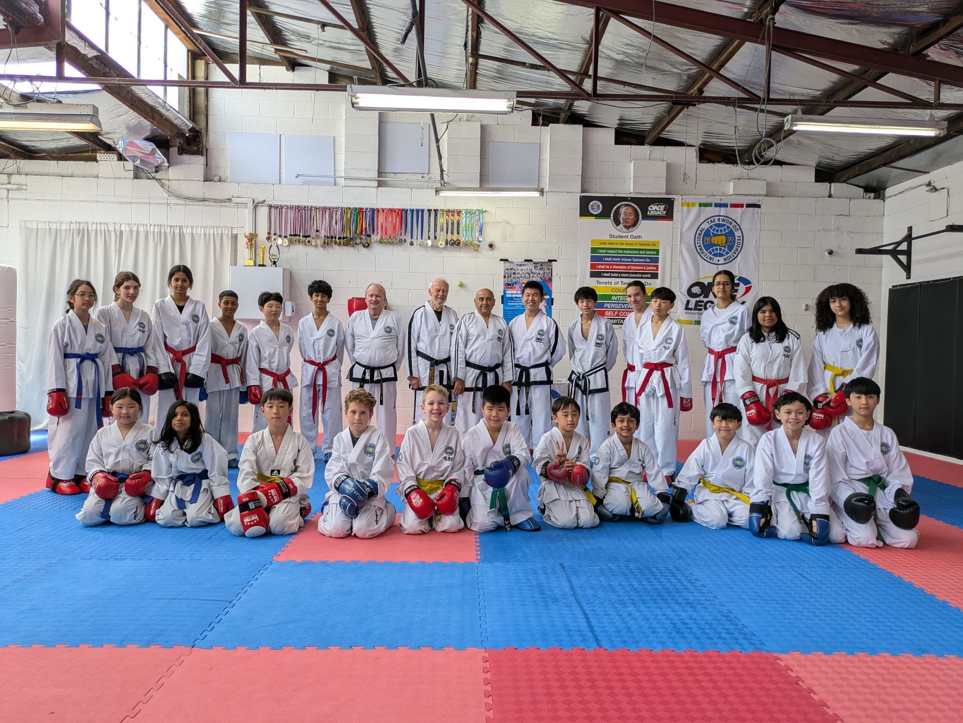 Martial arts class group photo in a dojo, with students in white uniforms posing on blue and red mats.