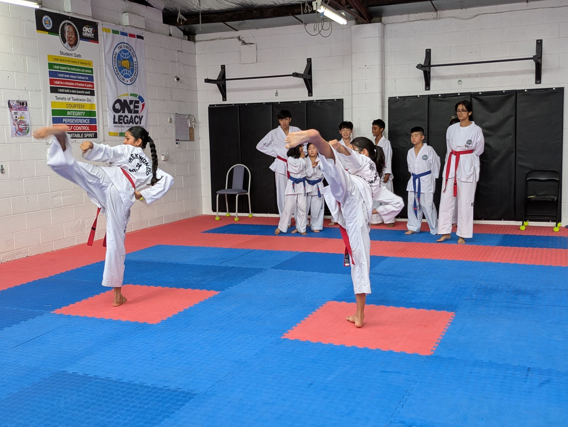 Children practicing kicks in a martial arts studio with blue and red mats and instructors watching