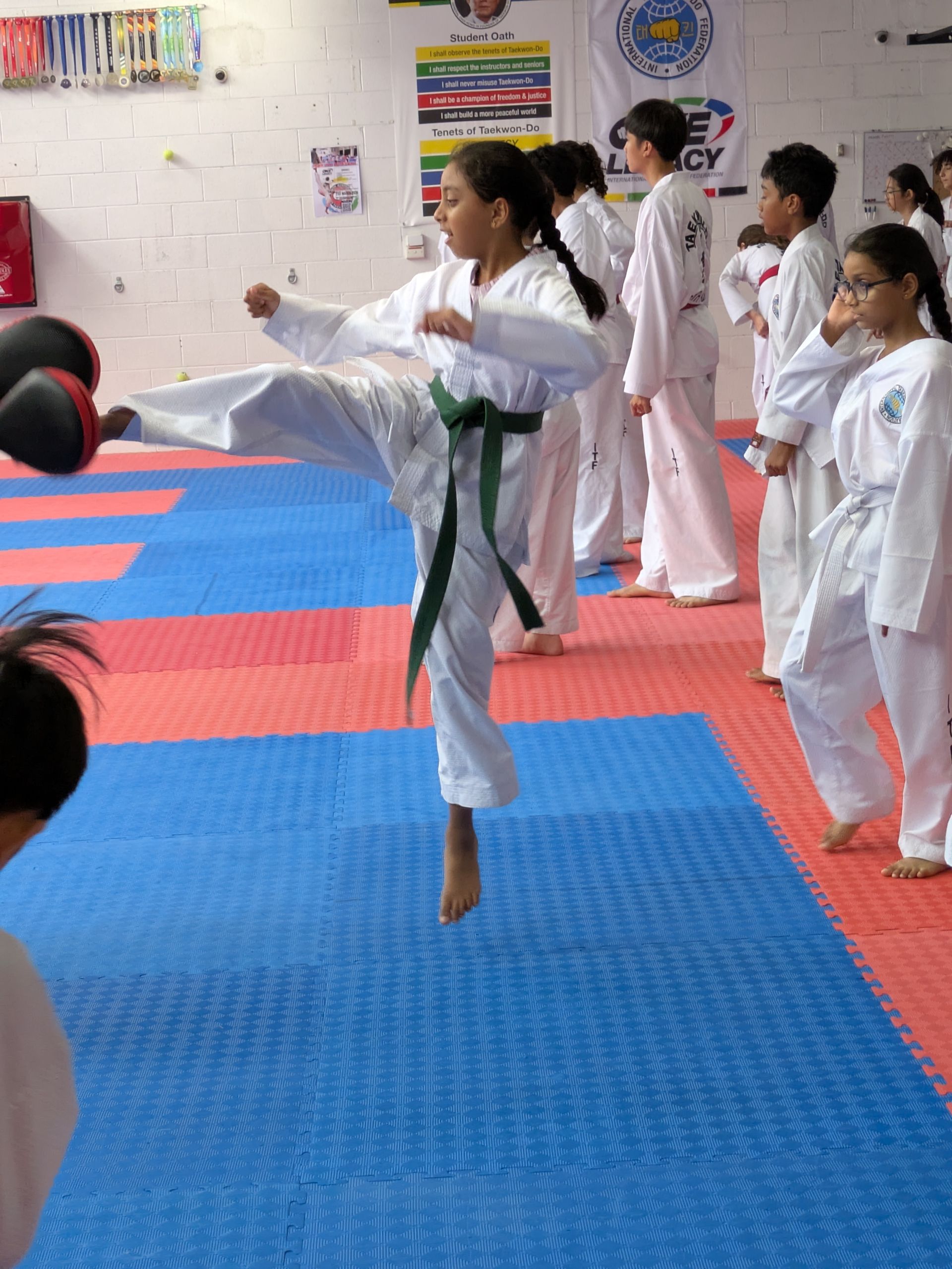 Martial arts students in white gis practicing kicks on blue and red mats indoors
