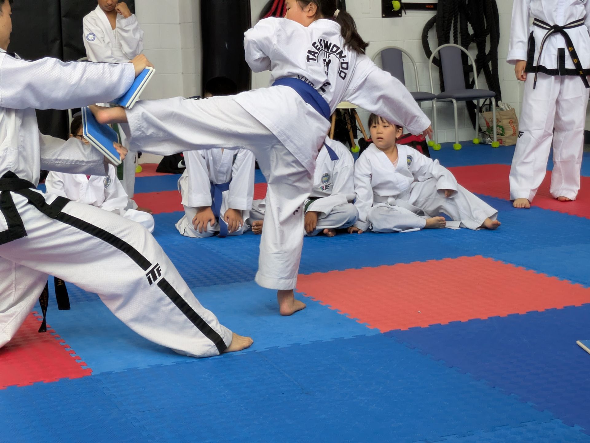 Martial arts class with students in white uniforms practicing kicks on red and blue mats