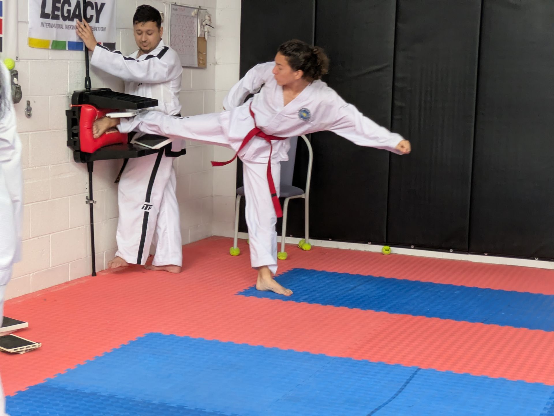 Martial arts practice with two people kicking and blocking on padded mats in a studio