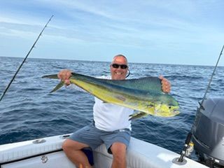 Man holding a large yellow-green fish on a boat at sea with fishing rods and calm water in the background