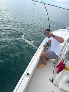 Person fishing from a boat, holding a fishing rod over calm water.