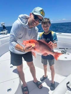 Two people on a boat holding a large red fish on a sunny day at sea