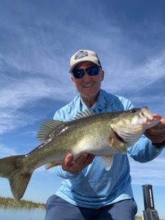 Smiling man in sunglasses holding a large fish against a bright blue sky