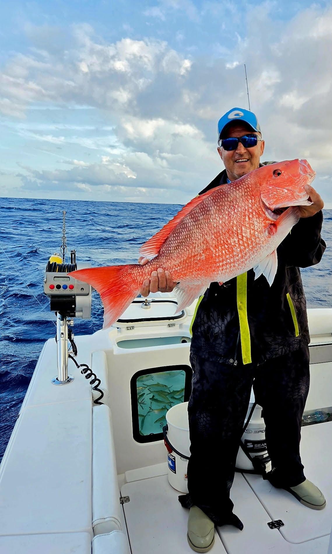 Angler on a boat holds a large red fish against a cloudy ocean backdrop