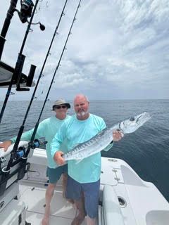 Two people on a boat holding a large fish on the open ocean
