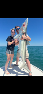 Two people on a boat holding a large fish against a blue ocean and sky