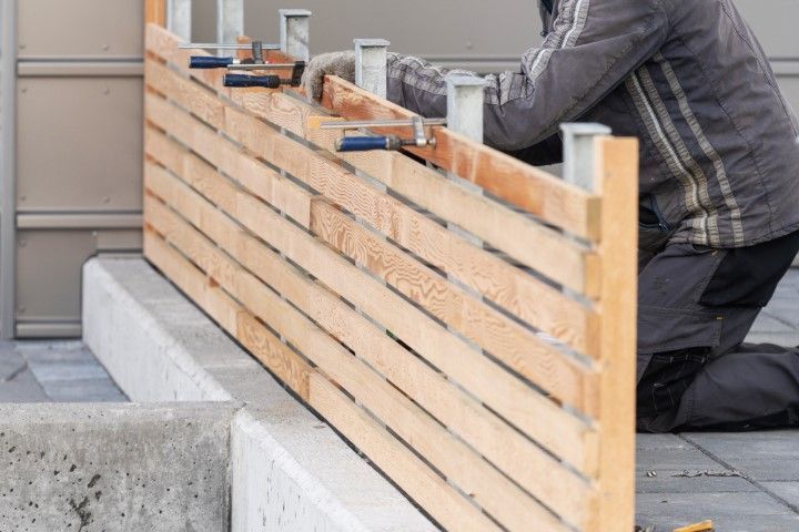 Person building a wood fence outdoors, using clamps to secure horizontal slats.