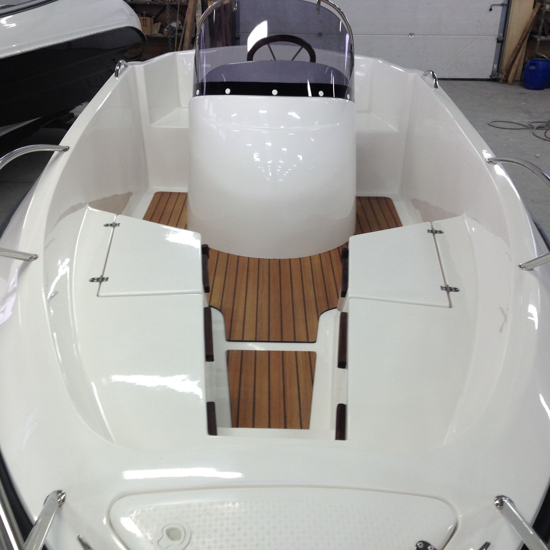 Een witte boot met een houten dek staat in een garage