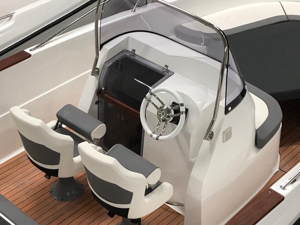 Een witte boot met een stuurwiel en twee stoelen op een houten dek.