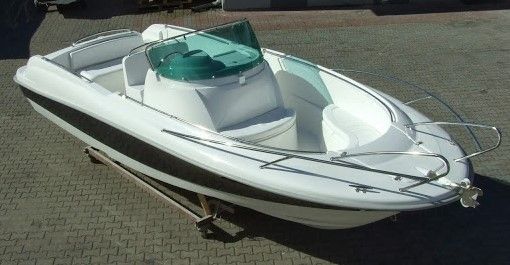 Een witte boot met een groene voorruit staat geparkeerd op een stoep van bakstenen