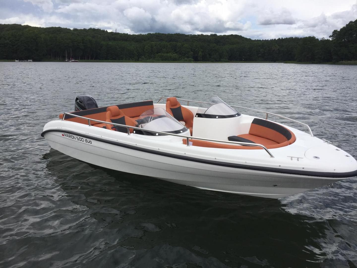 Een wit en oranje boot drijft op een meer.