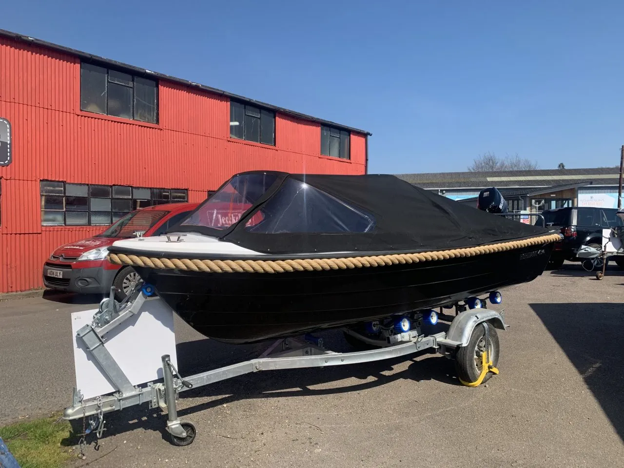 Een zwarte boot ligt op een trailer voor een rood gebouw.