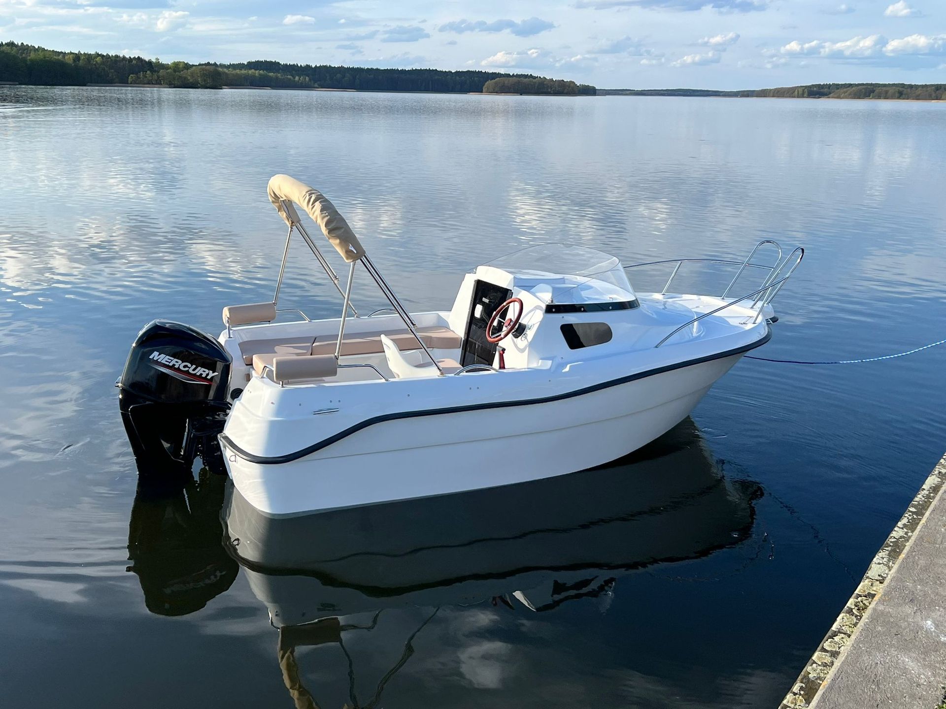 Een kleine witte boot ligt aangemeerd in het water bij een steiger.