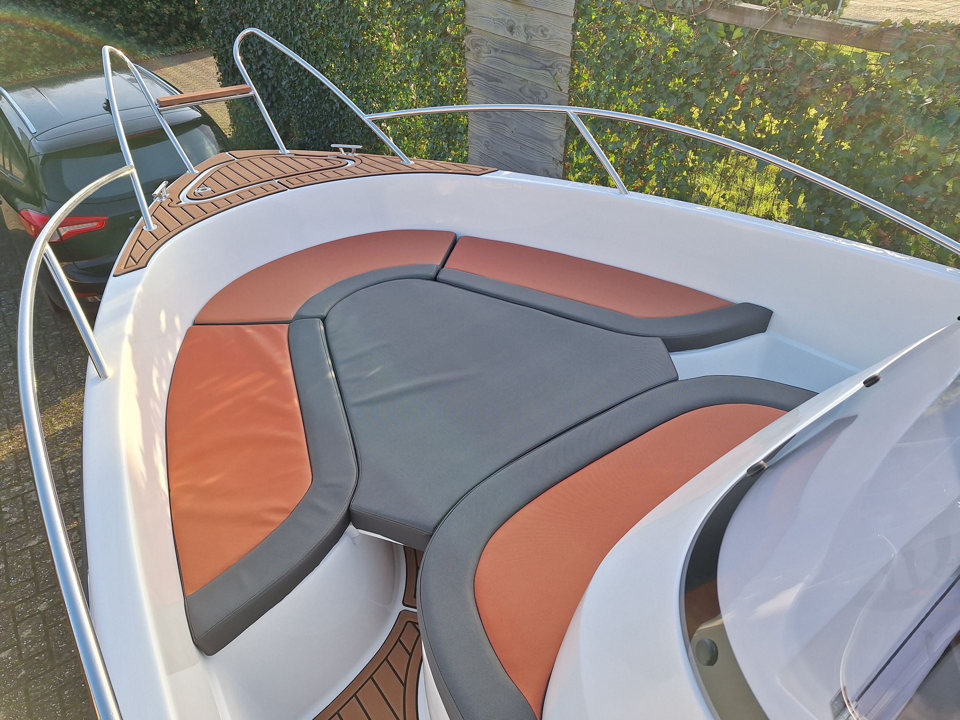 Een boot met oranje en zwarte stoelen ligt naast een auto.