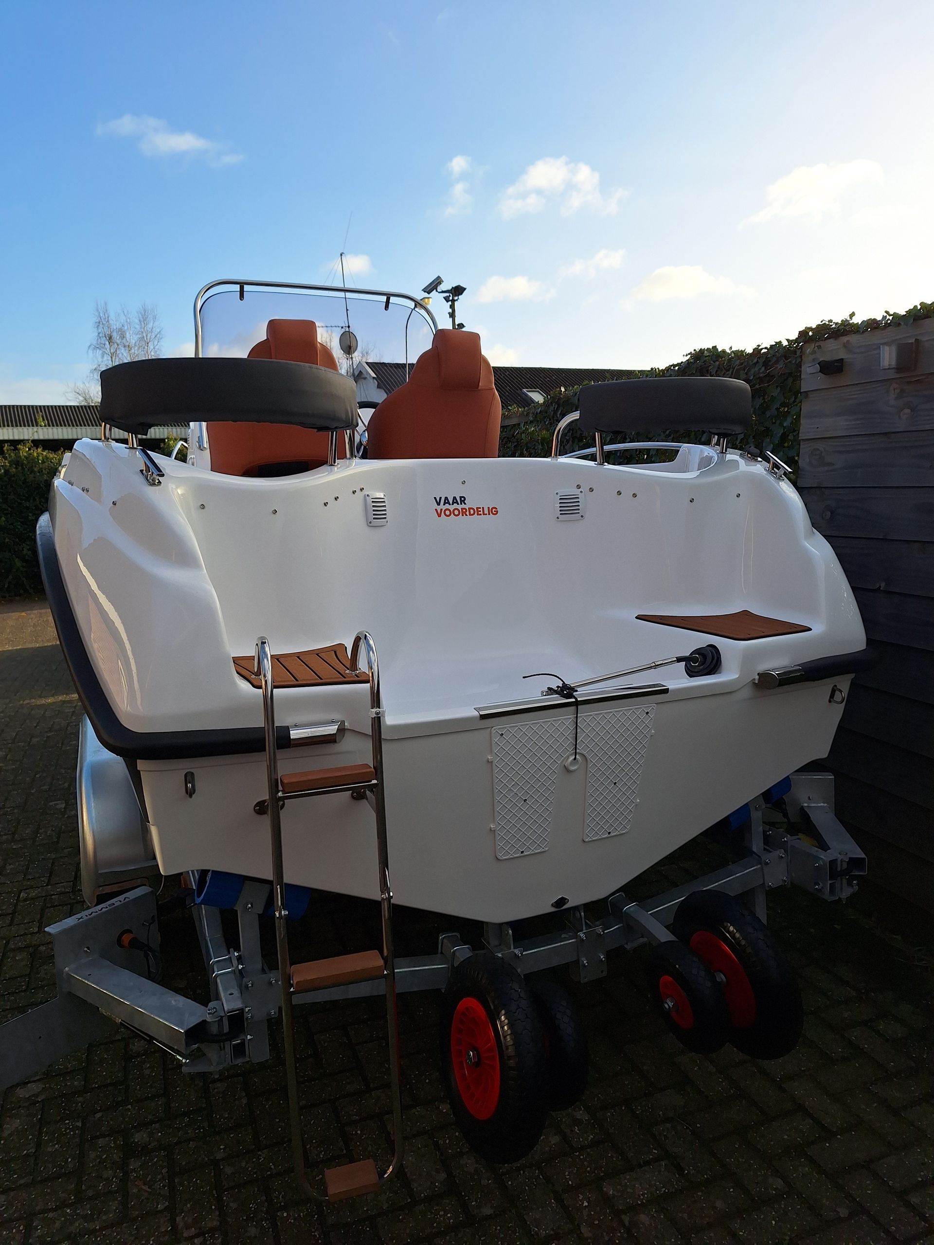 Een witte boot staat op een aanhanger met rode wielen.