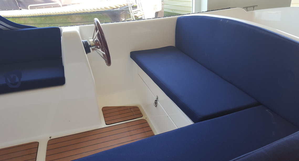 De binnenkant van een boot met blauwe kussens en een stuurwiel.