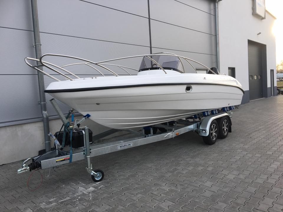 Een witte boot staat op een trailer voor een gebouw geparkeerd.