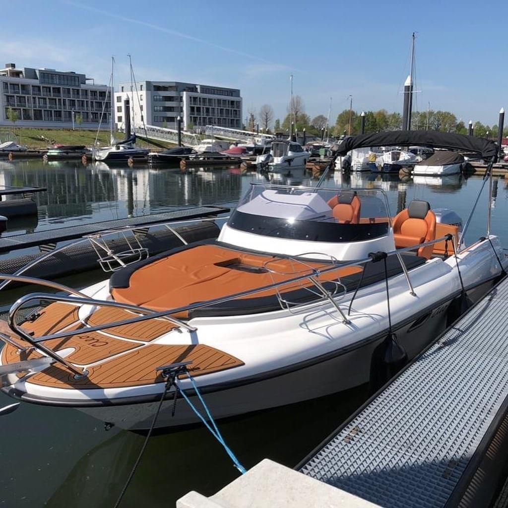Een wit-oranje boot ligt aangemeerd in een jachthaven.