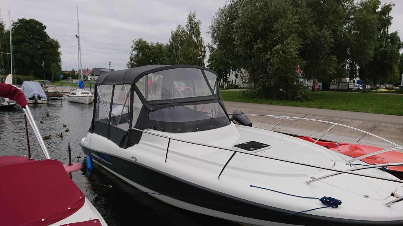 Een witte boot met een zwarte kap ligt aangemeerd in een haven.