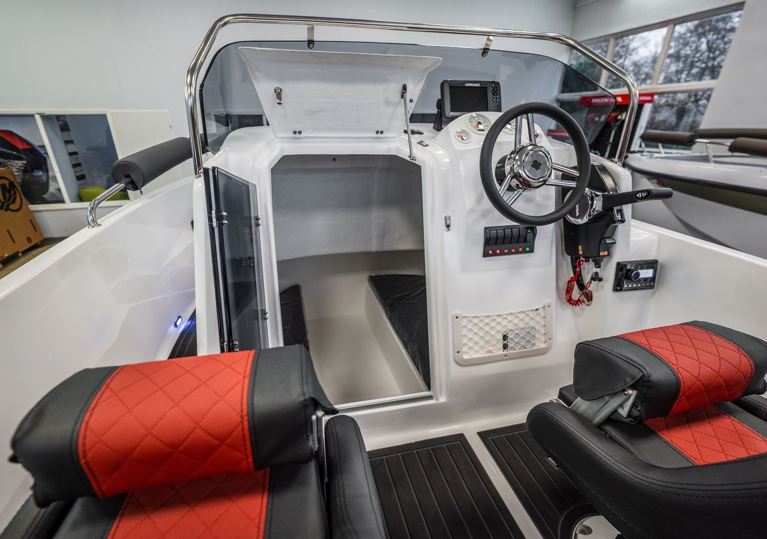De binnenkant van een boot met rode en zwarte stoelen en een stuurwiel.