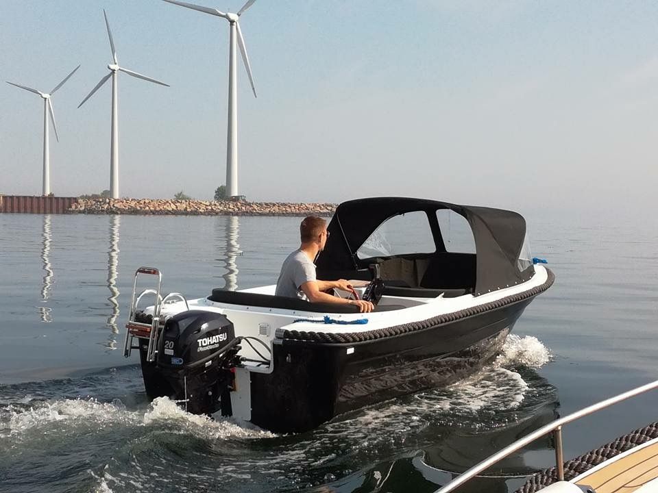 Een man bestuurt een boot in het water met windmolens op de achtergrond
