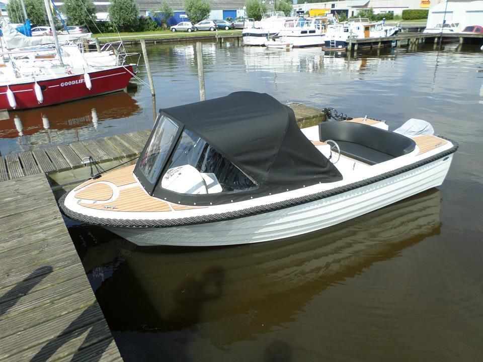 Een kleine boot ligt aangemeerd aan een steiger naast een watermassa.