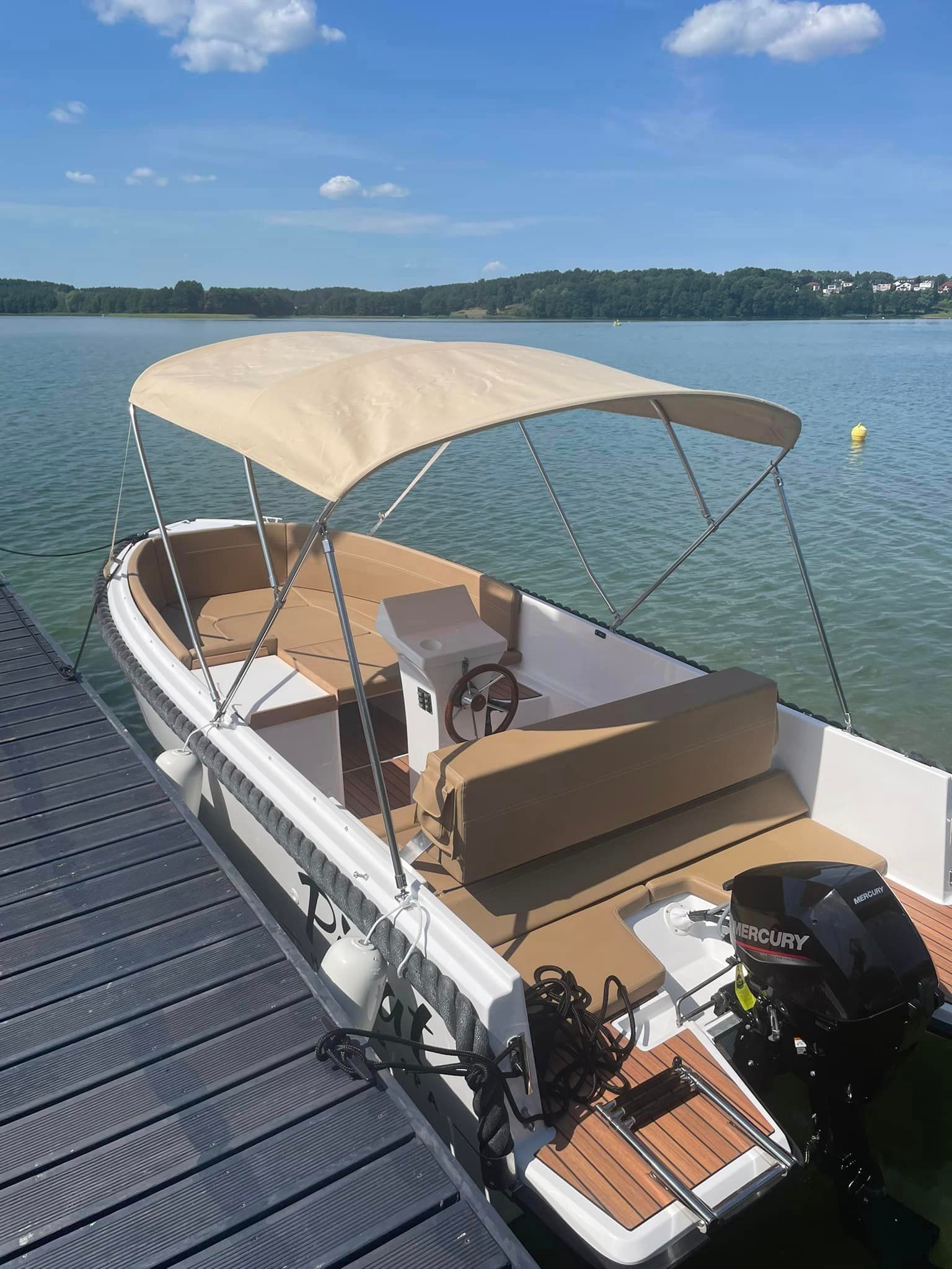 Een boot met een luifel ligt aangemeerd aan een steiger aan een meer.