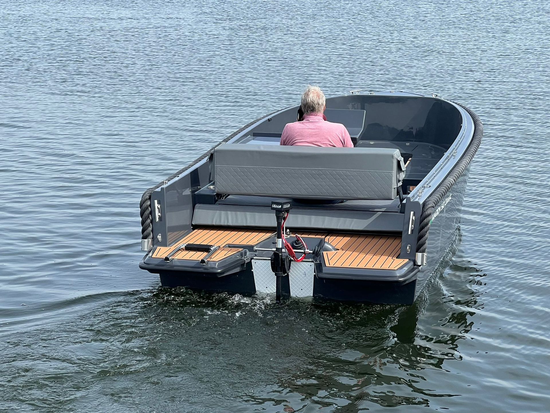 Een man zit op de achterkant van een boot in het water.