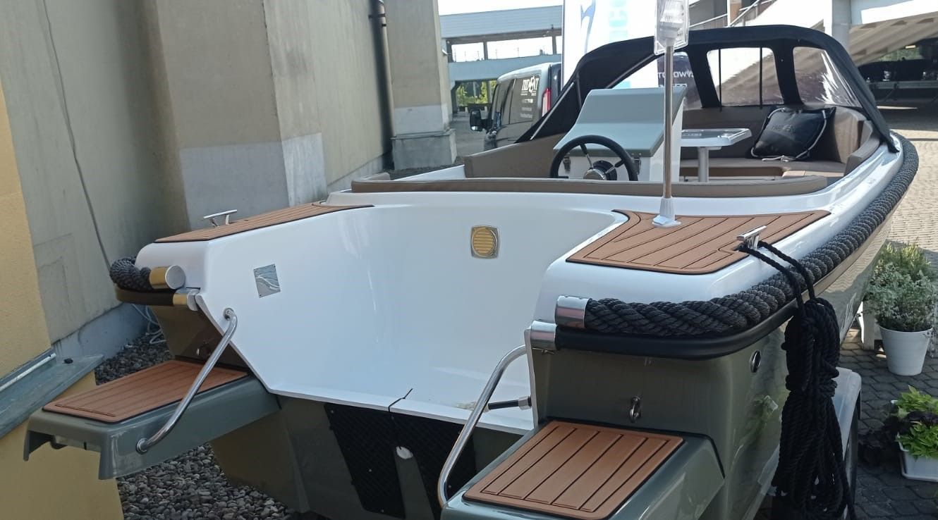 Een witte boot met houten dekken ligt voor een gebouw geparkeerd.