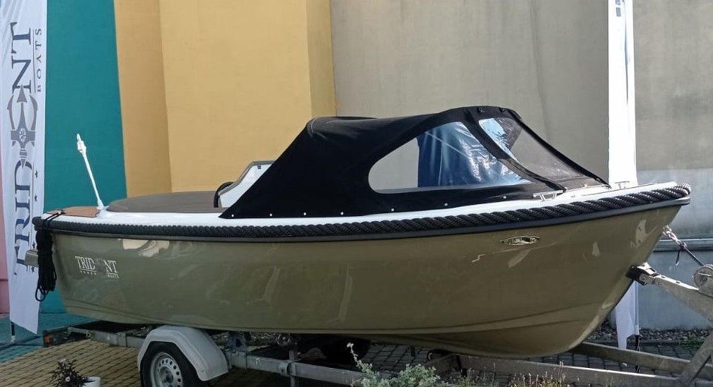 Een kleine boot ligt op een trailer voor een gebouw.