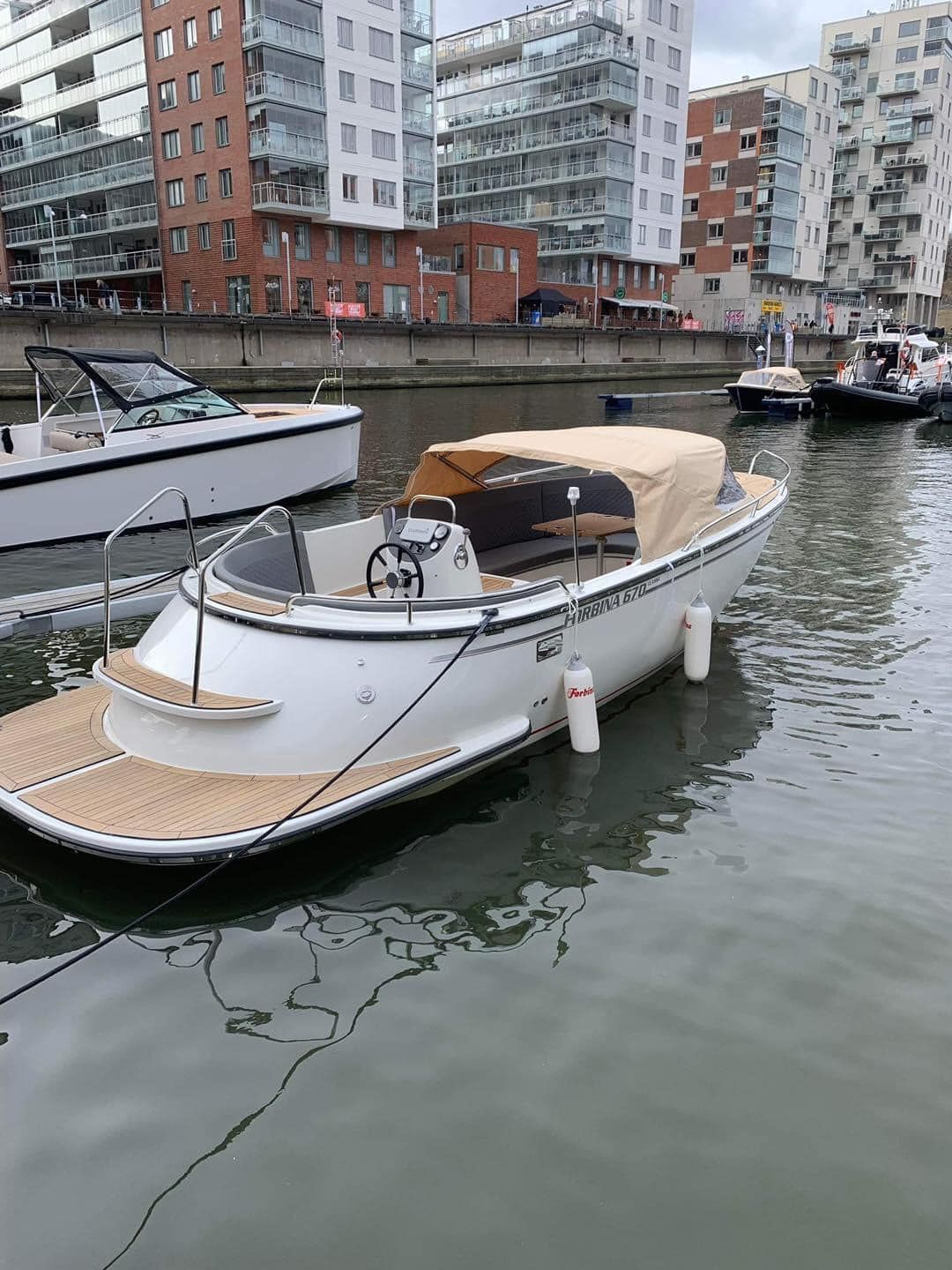 Een witte boot met een houten dek ligt aangemeerd in een haven.