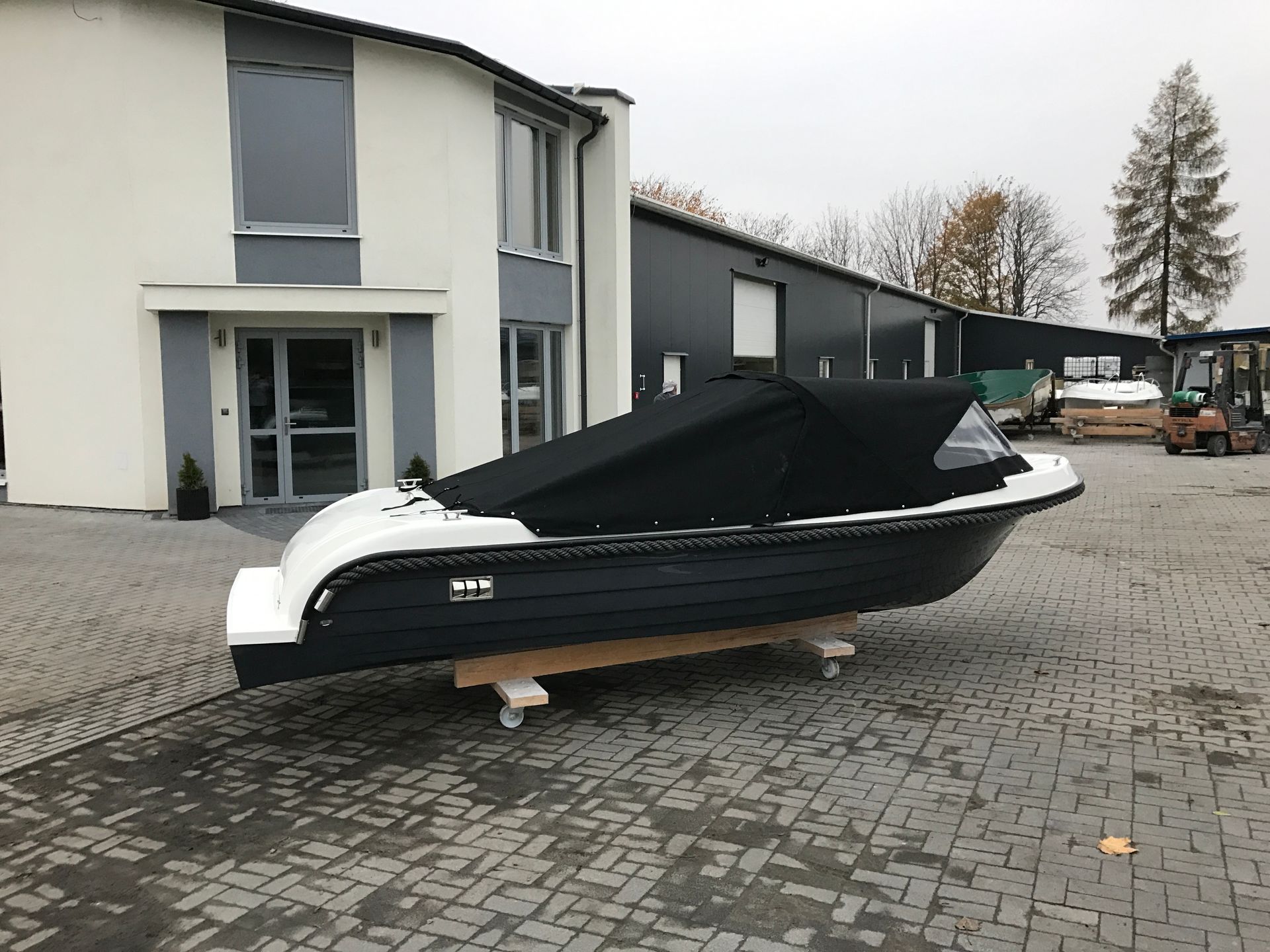 Een boot met een zwart dekzeil ligt voor een gebouw geparkeerd.