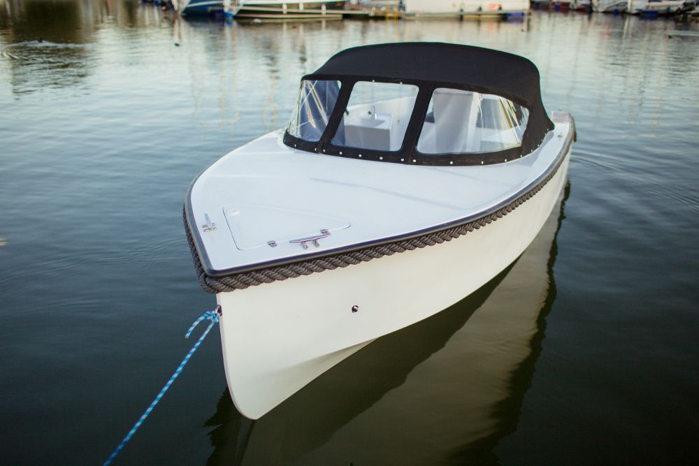 Een kleine witte boot met een zwarte kap drijft op het water.