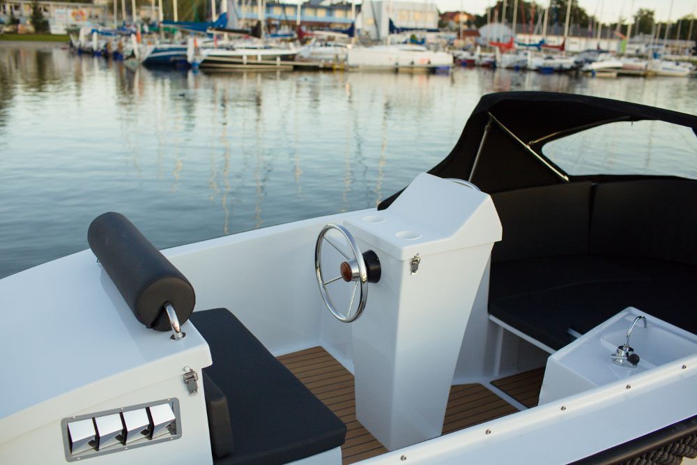Een witte boot met een zwart dak ligt aangemeerd in een haven.