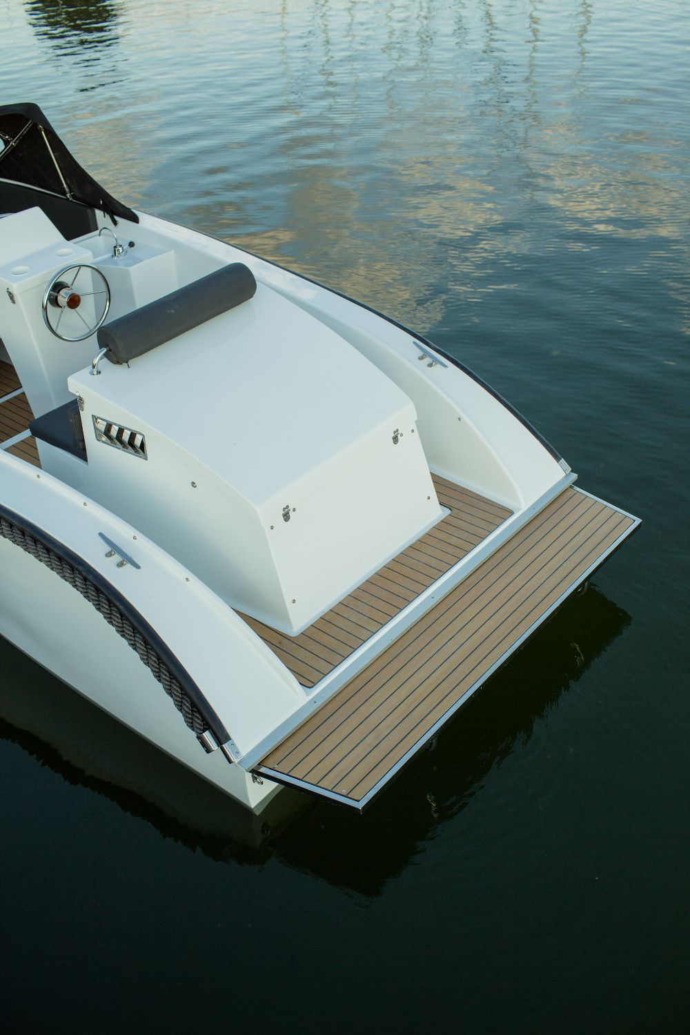 Een witte boot met een houten dek drijft op een watermassa.