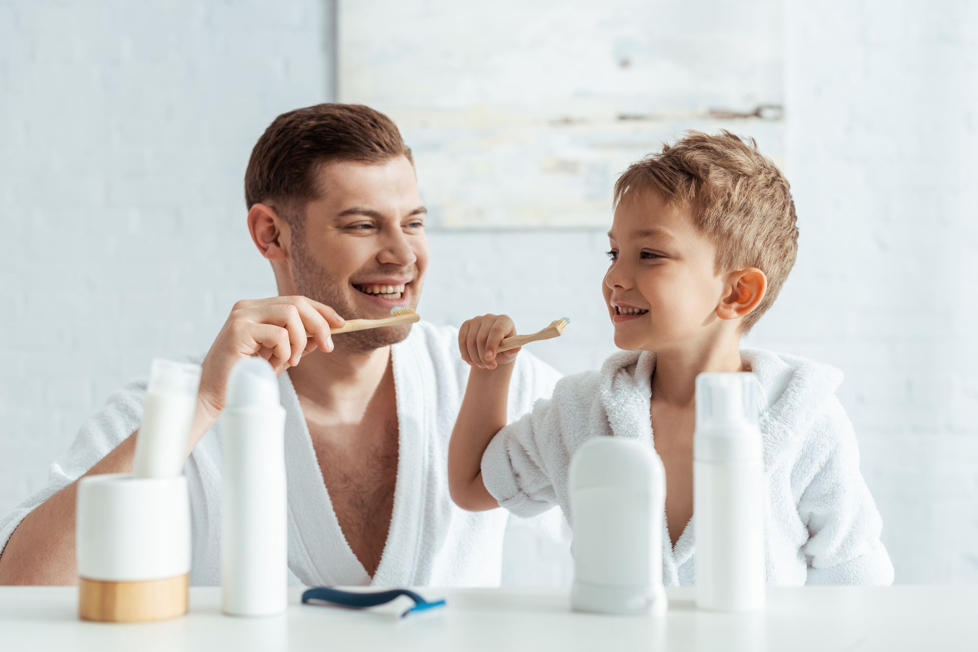 A man and a boy are brushing their teeth together at a table.