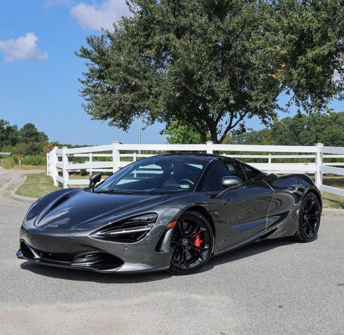 Sleek black sports car parked on a sunny road beside a white fence and tree